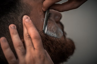 Close-up of barber shaving man's beard with straight razor