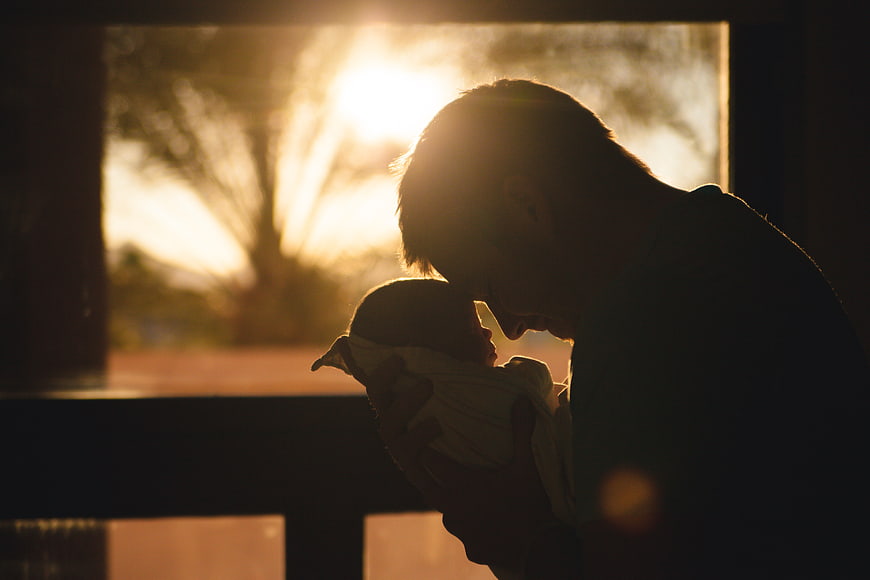 Silhouette of Father Holding Newborn Baby in Golden Sunlight