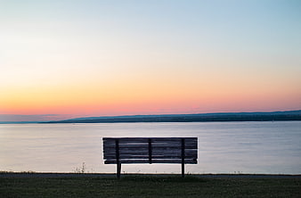 Empty wooden bench overlooking calm lake at sunset