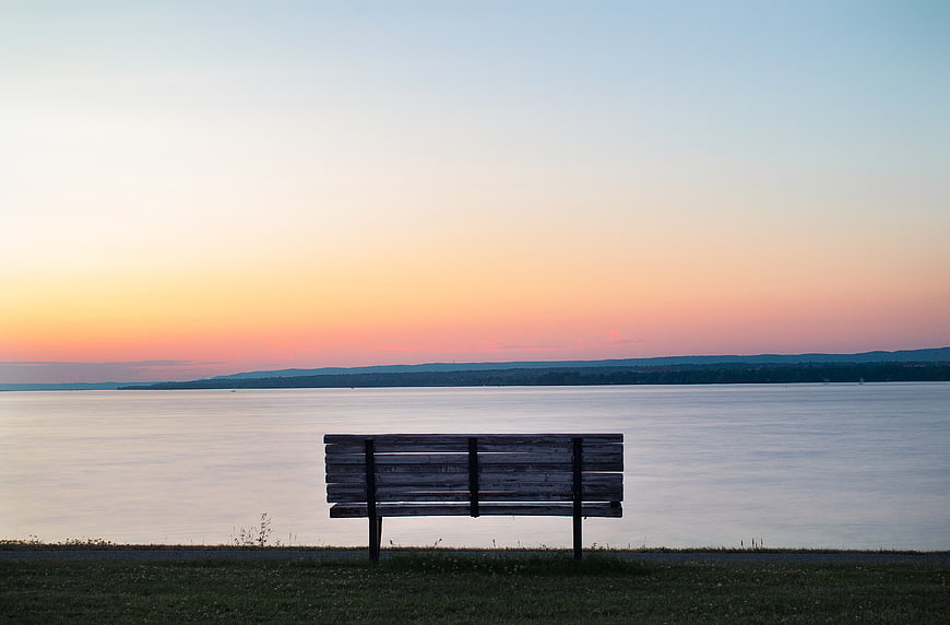 Empty wooden bench overlooking calm lake at sunset