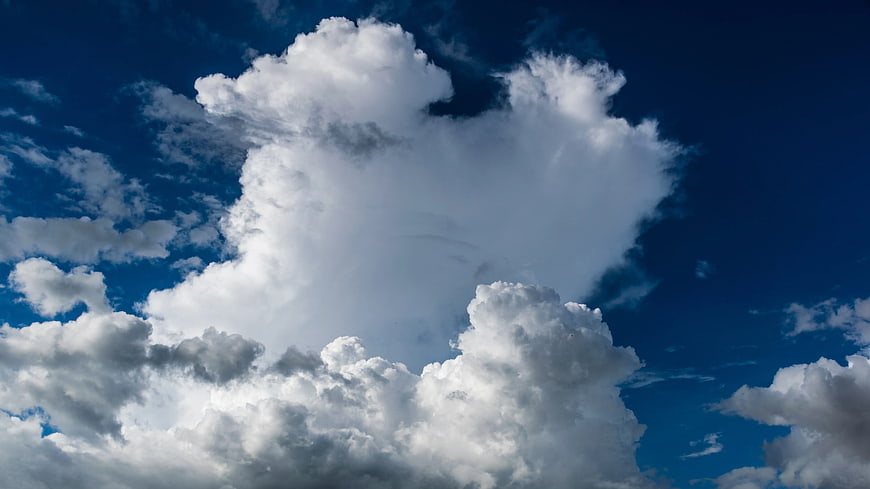 Dramatic white cumulus clouds against deep blue sky