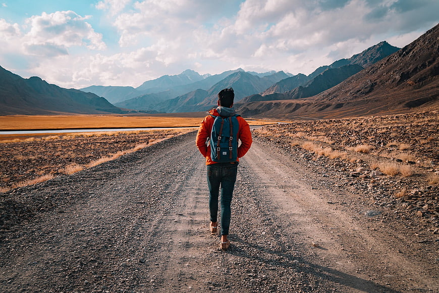 Hiker Walking on Gravel Road in Mountain Landscape