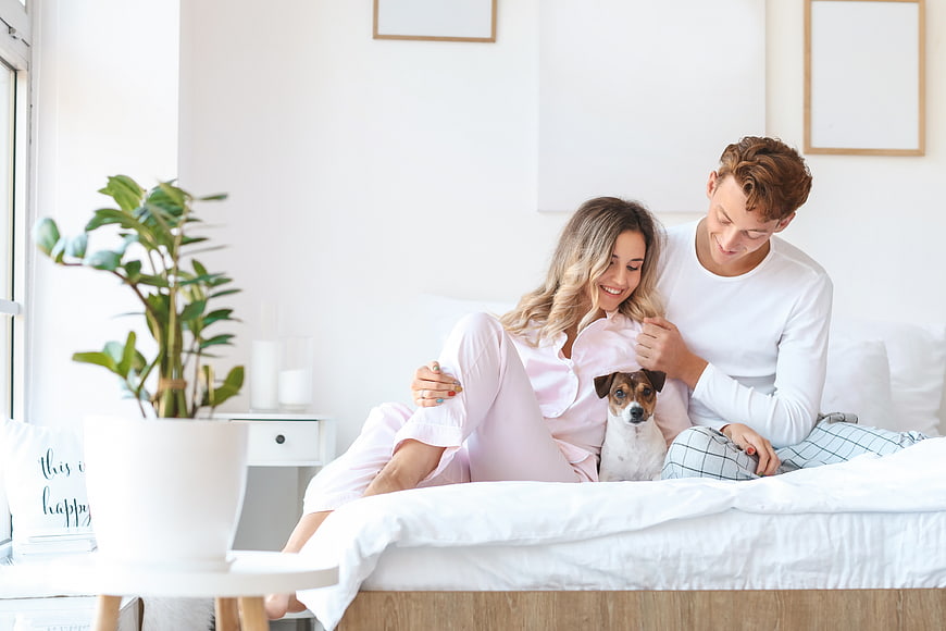 Happy young couple relaxing in bed with their dog