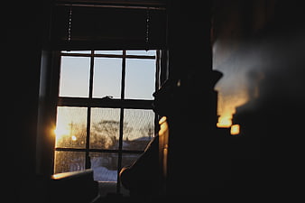 Silhouette of person looking out window at sunset