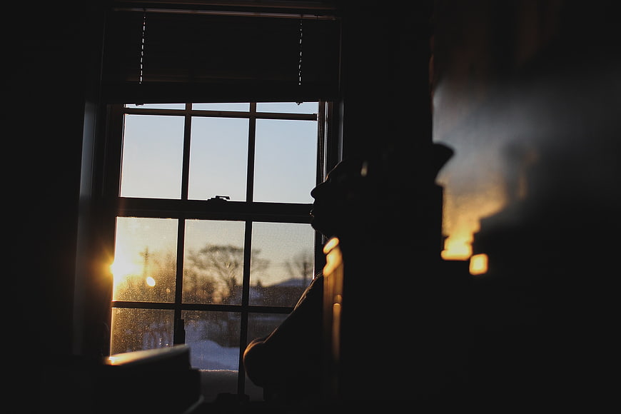 Silhouette of person looking out window at sunset