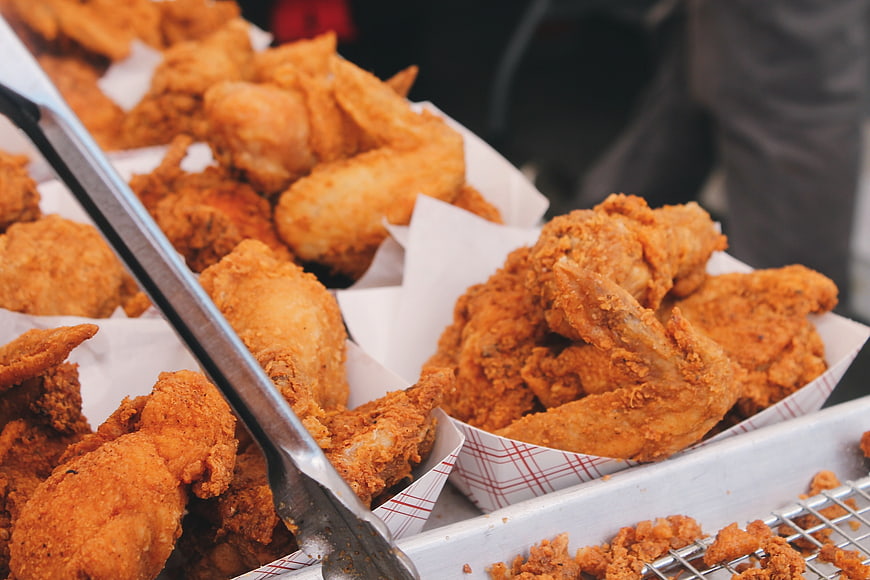 Crispy fried chicken wings in paper trays with tongs