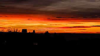 Vibrant orange sunset over silhouetted landscape with house