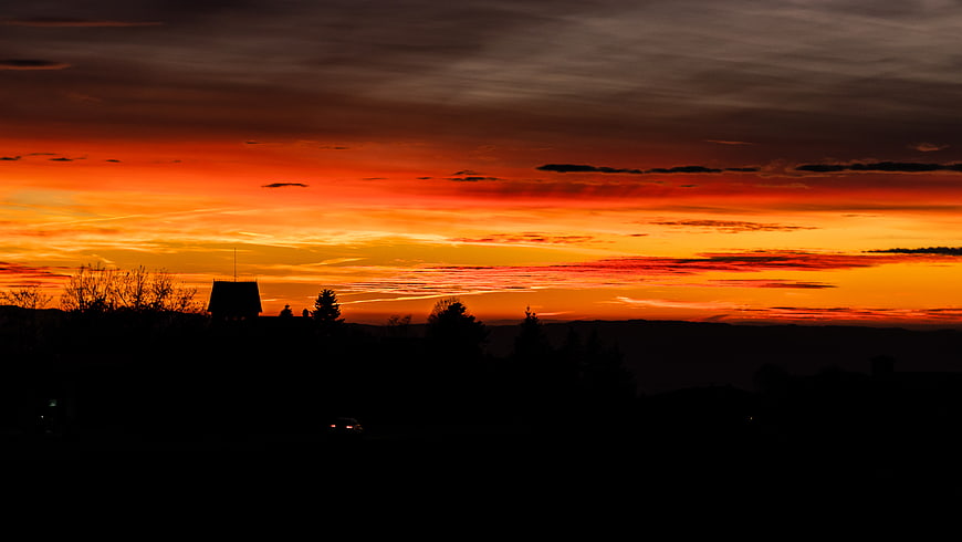 Vibrant orange sunset over silhouetted landscape with house