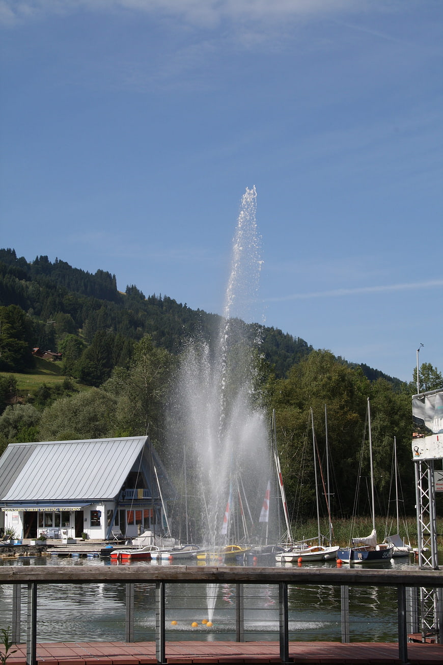 Fountain spraying water at lake marina with boats and mountains
