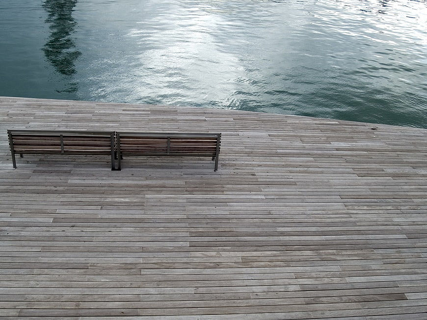 Empty wooden bench on waterfront boardwalk with rippling water