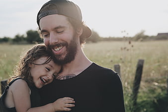 Happy father hugging smiling daughter in sunny field