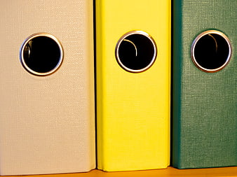 Close-up of beige, yellow, and green ring binders on a shelf