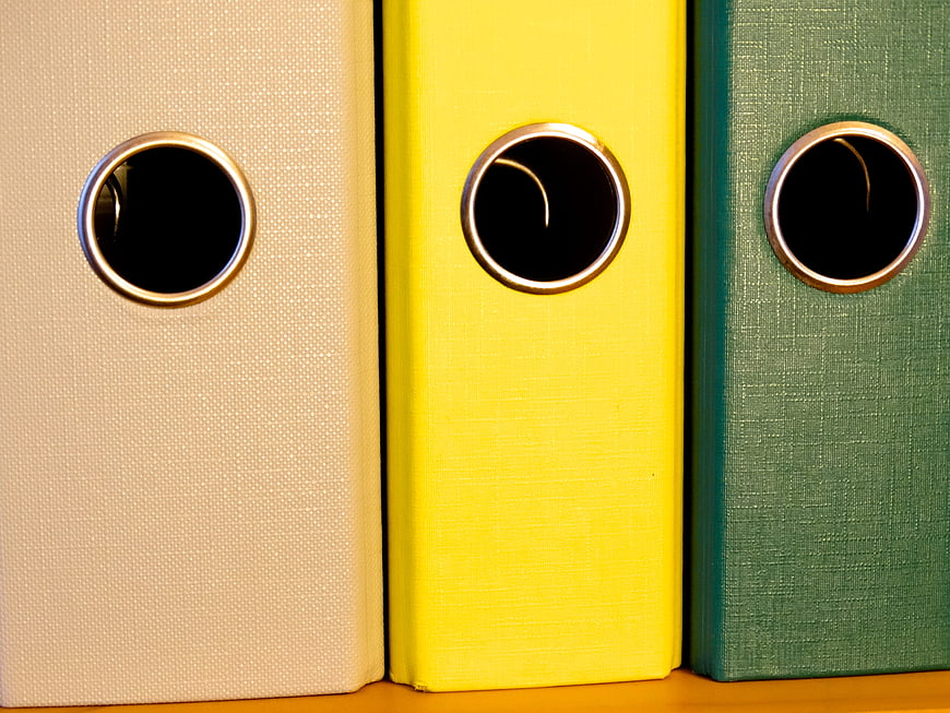 Close-up of beige, yellow, and green ring binders on a shelf
