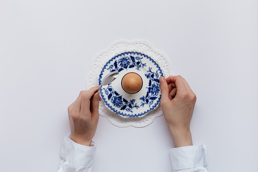 Top view of hands holding blue and white plate with egg