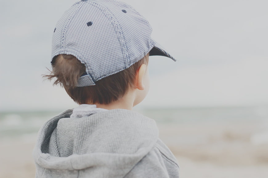 Toddler Boy in Cap Looking at Ocean Beach
