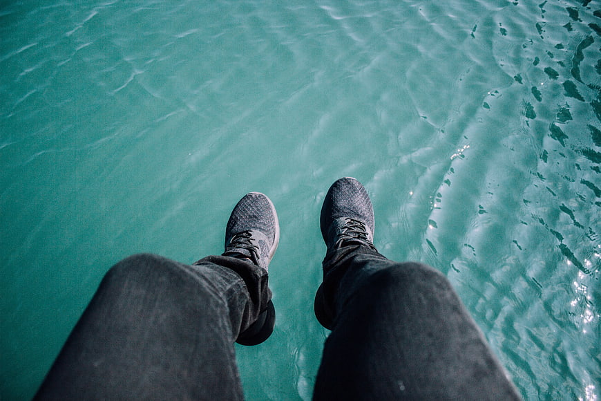 First-person view of feet in sneakers over turquoise pool water