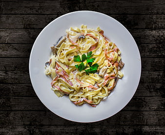 Top View of Tagliatelle Pasta with Ham, Mushrooms, and Parsley on White Plate