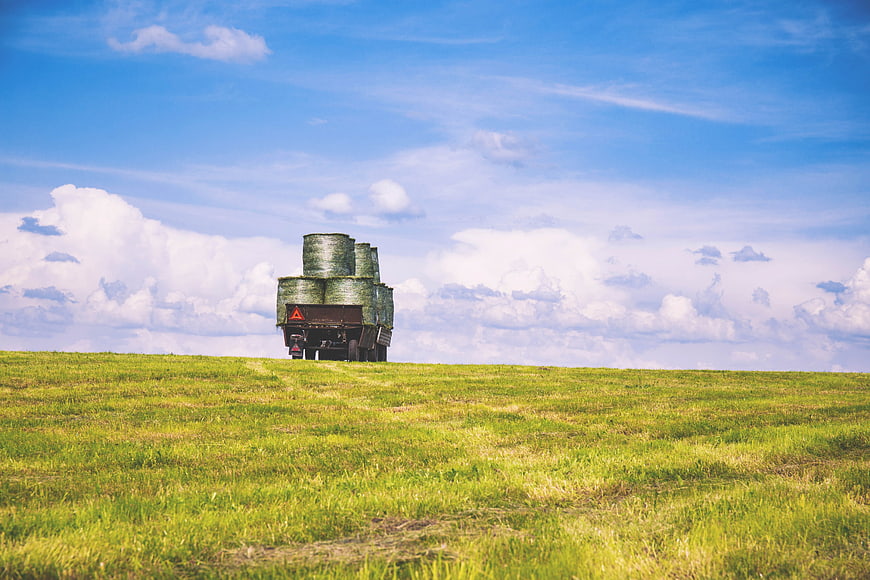 Truck carrying hay bales on green field horizon