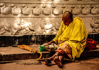 Hindu Monk in Yellow Robes Sitting by Temple Carvings
