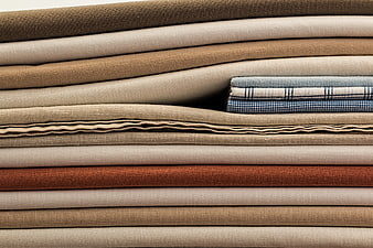 Stack of folded beige and brown linen fabrics with blue plaid accent