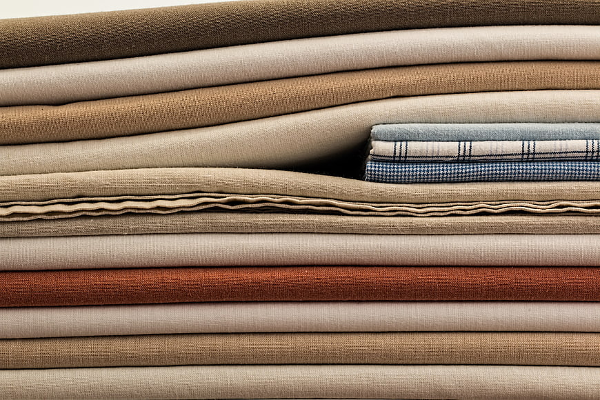 Stack of folded beige and brown linen fabrics with blue plaid accent