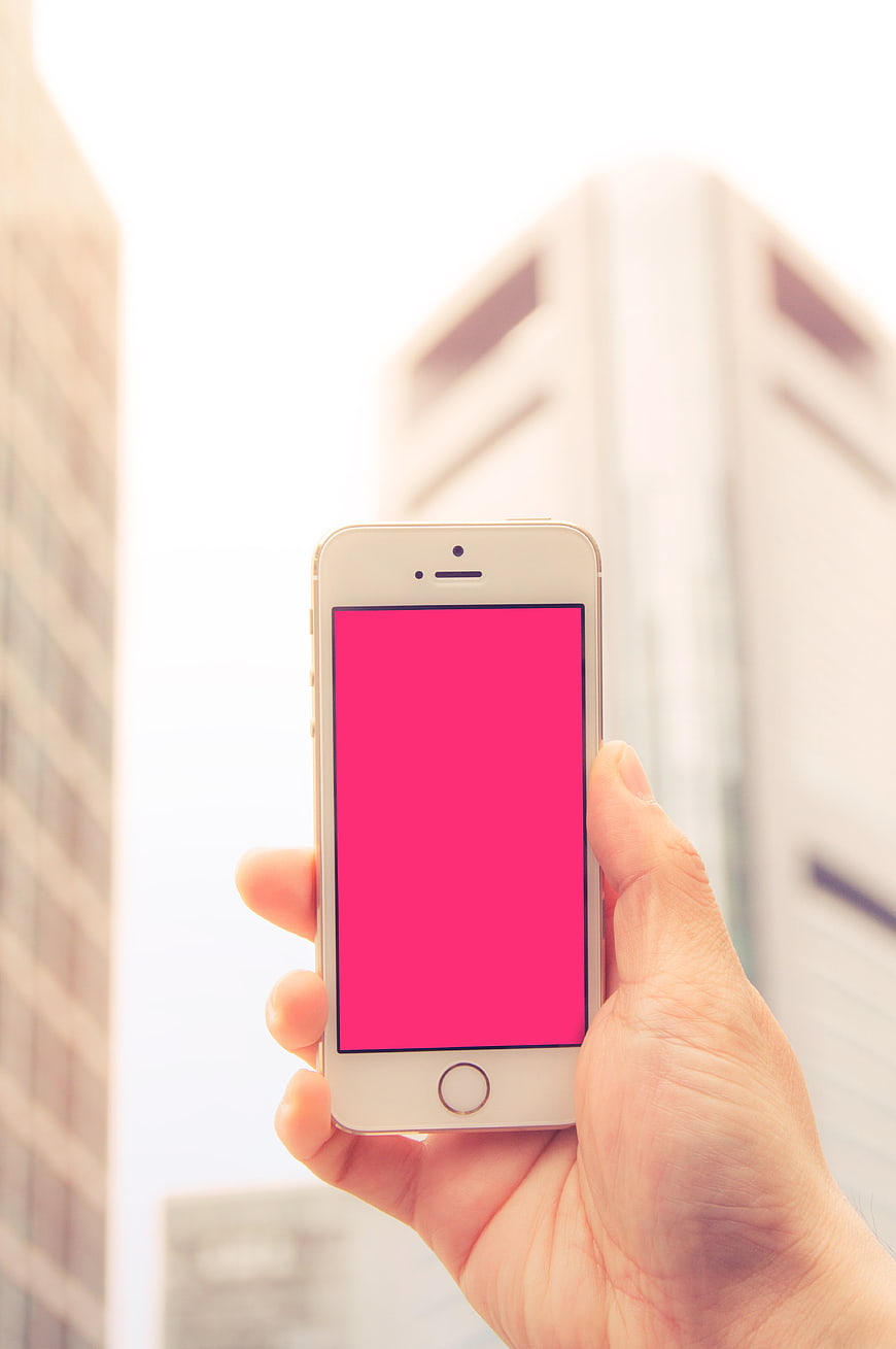 Hand holding smartphone with pink screen against blurred city buildings