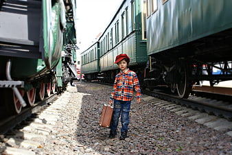Young boy with vintage suitcase standing between old green trains