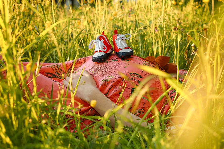 Pregnant Woman Lying In Grass With Baby Shoes