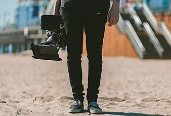 Filmmaker holding professional cinema camera on sandy beach