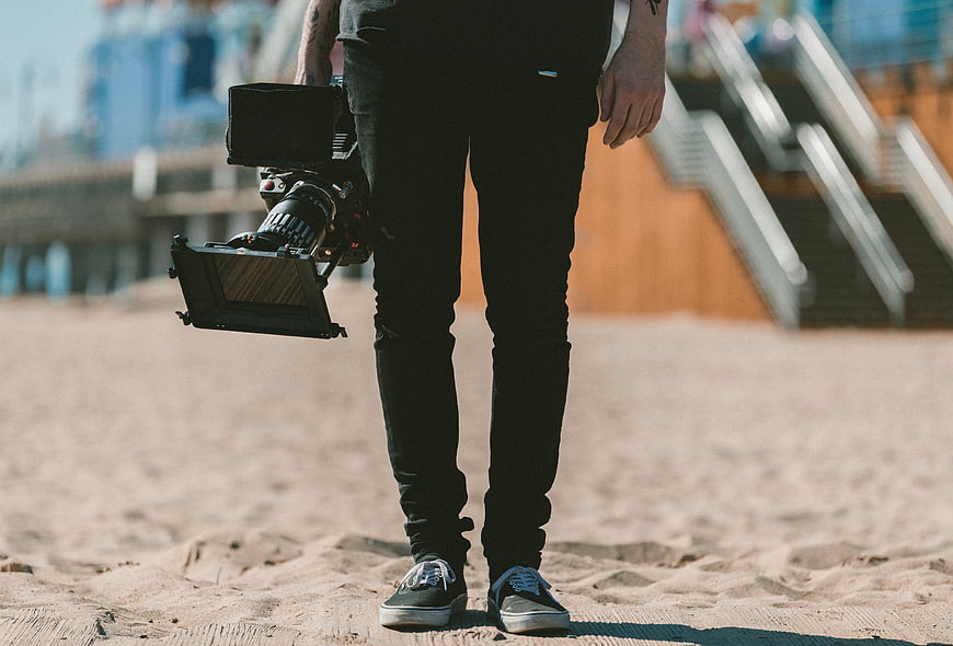 Filmmaker holding professional cinema camera on sandy beach
