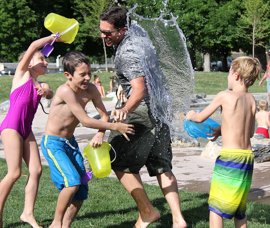 Children splashing water on father during summer play