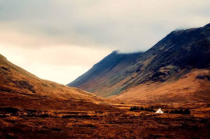 Solitary white cottage in rugged mountain valley landscape