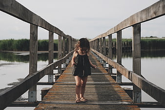 Little girl walking on wooden bridge over lake