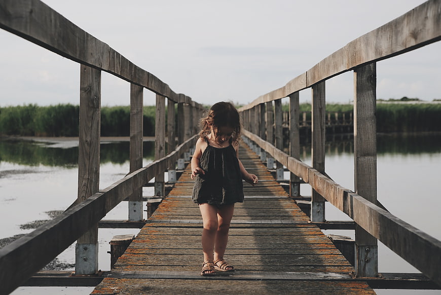 Little girl walking on wooden bridge over lake