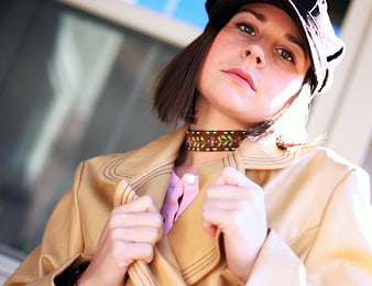Woman in beige coat and hat looking up in sunlight