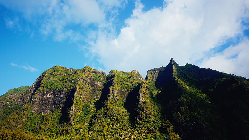 Lush Green Mountain Peaks Under Blue Sky with Clouds