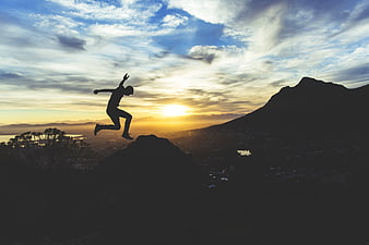 Silhouette of man jumping on mountain peak at sunset