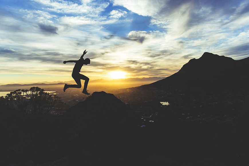 Silhouette of man jumping on mountain peak at sunset