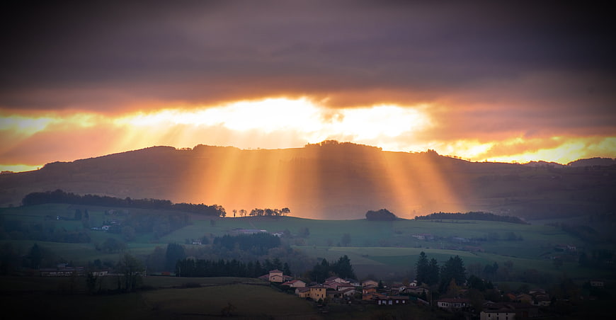 Dramatic Sun Rays Breaking Through Clouds Over Rolling Hills