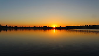 Serene Sunset Over Calm Lake with Silhouetted Trees
