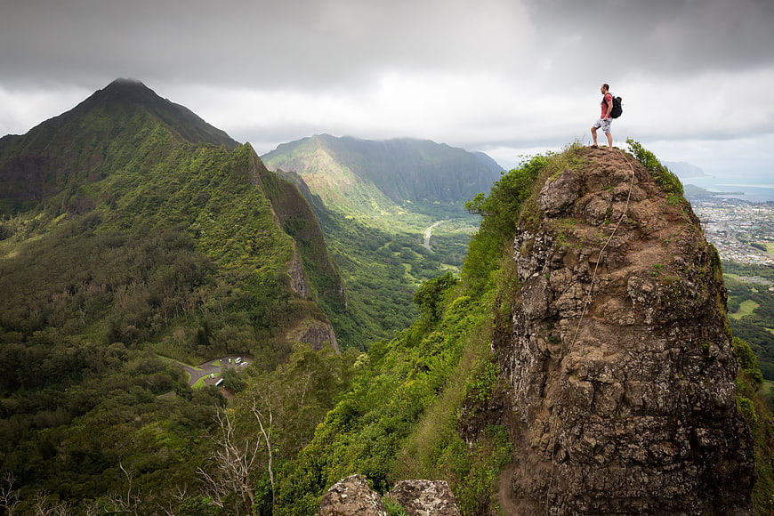 Hiker standing on rocky mountain peak overlooking lush green valley