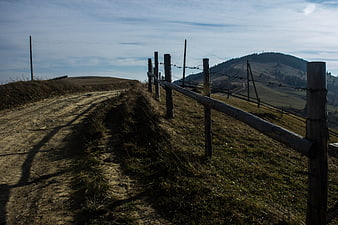 Rural dirt road with wooden fence leading to mountain landscape