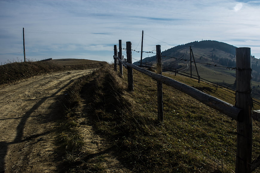 Rural dirt road with wooden fence leading to mountain landscape