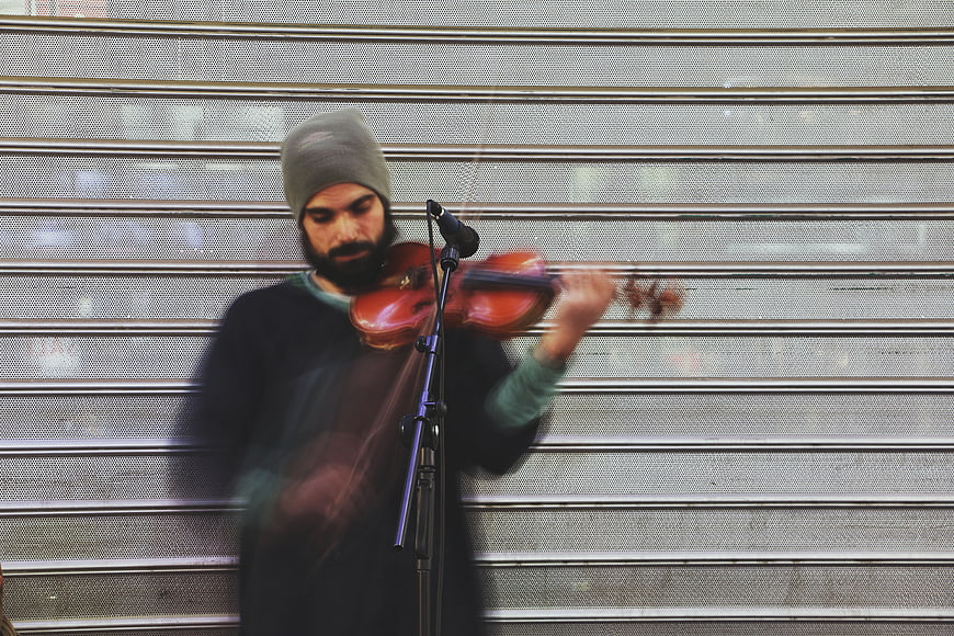 Bearded man playing violin on street with motion blur