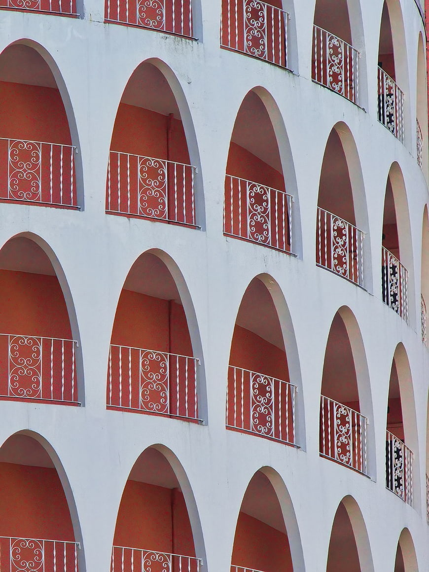 White building facade with repeating red arched balconies