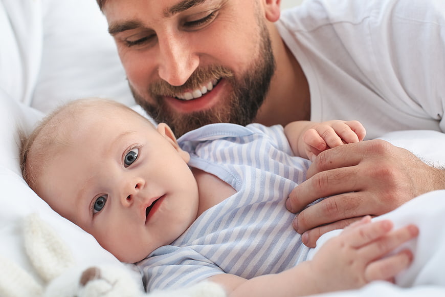 Happy Father Smiling at Baby in Bed