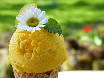 Yellow ice cream cone garnished with daisy and mint leaf outdoors
