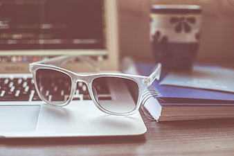 White sunglasses on laptop with notebook and coffee cup