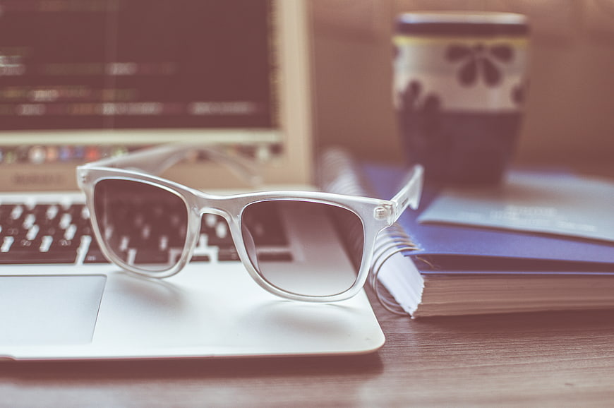 White sunglasses on laptop with notebook and coffee cup