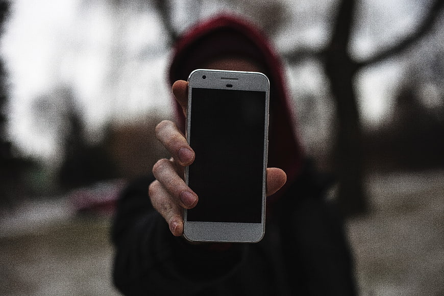 Person in Hoodie Holding Smartphone in Forest